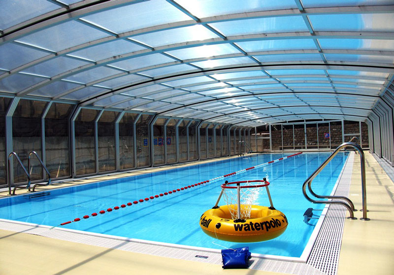 A pool enclosure over a large pool with a water polo net