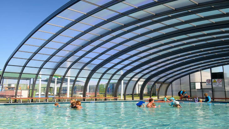 A large commercial pool enclosure with people swimming underneath